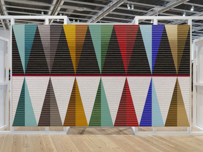 Large textile artwork with rows of colorful triangles pointing up and down, displayed in a modern gallery space.