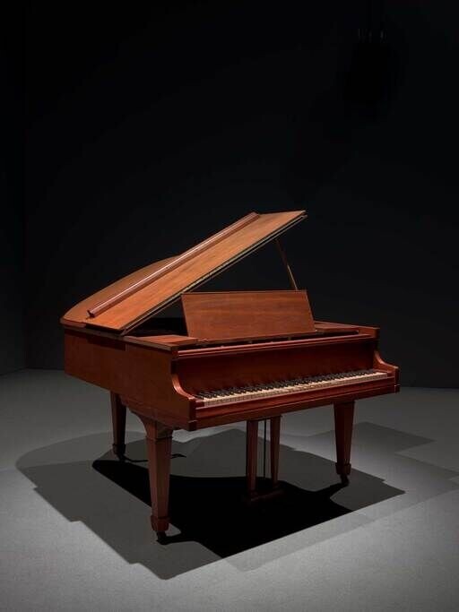 A grand piano with a closed lid stands in a dimly lit room.