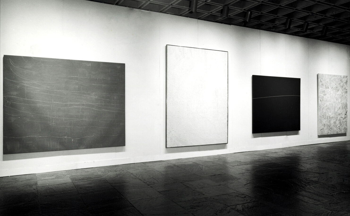 Black-and-white photograph of works of art hanging in a gallery.