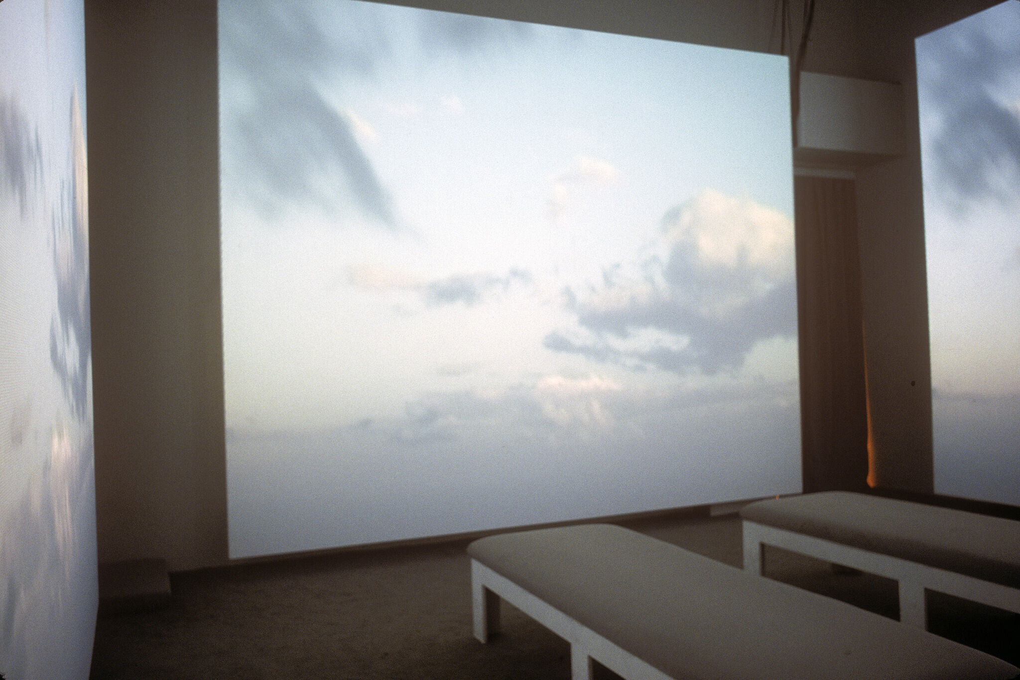 A gallery with walls covered in a projection of a sky with clouds.