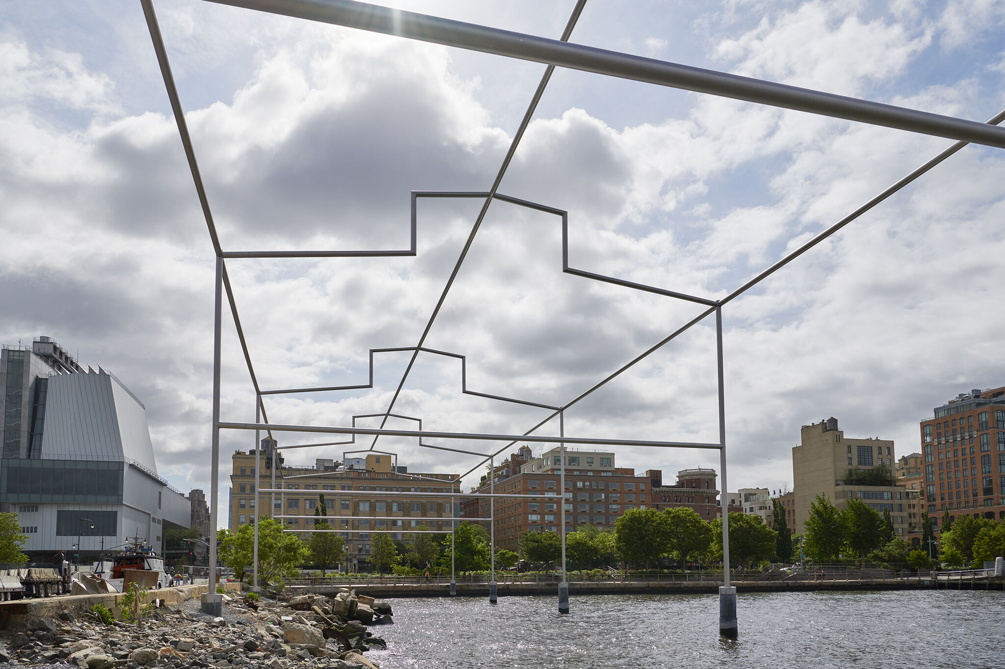 Close-up view of Day's End steel sculpture against a bright, cloudy sky with the Manhattan skyline in the background.