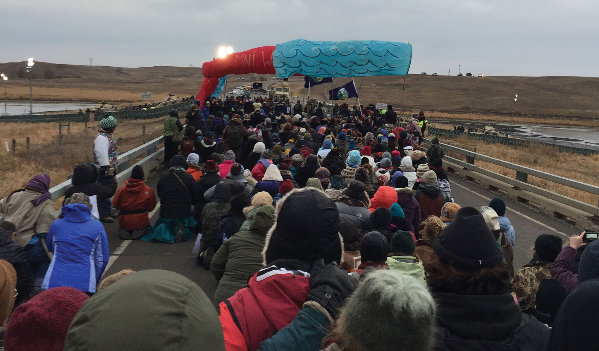 Protesters kneeling and standing across a road and waving banners.