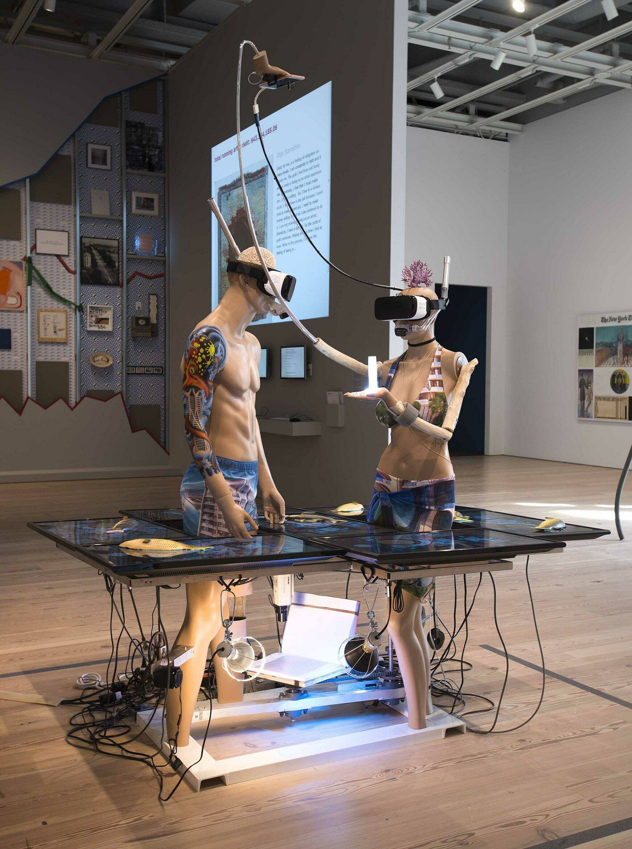 Two sculptures of figures wearing VR headsets displayed in a gallery.