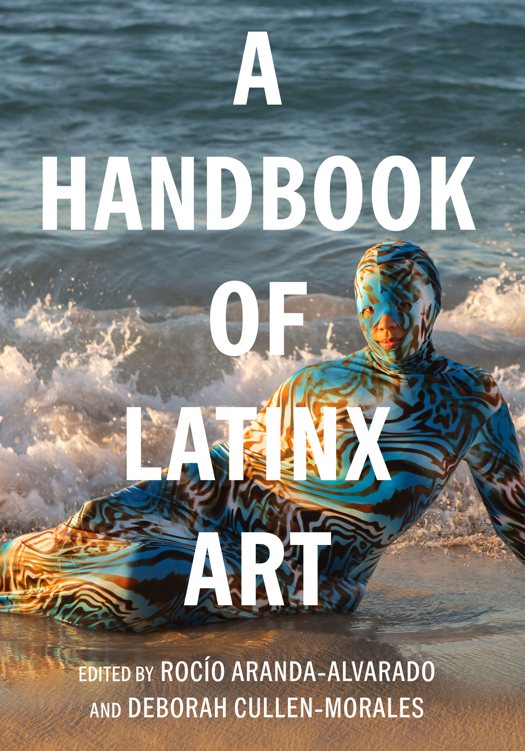 Person in a colorful bodysuit lies on a beach with waves in the background. Text reads: "A Handbook of Latinx Art," edited by Rocío Aranda-Alvarado and Deborah Cullen-Morales.