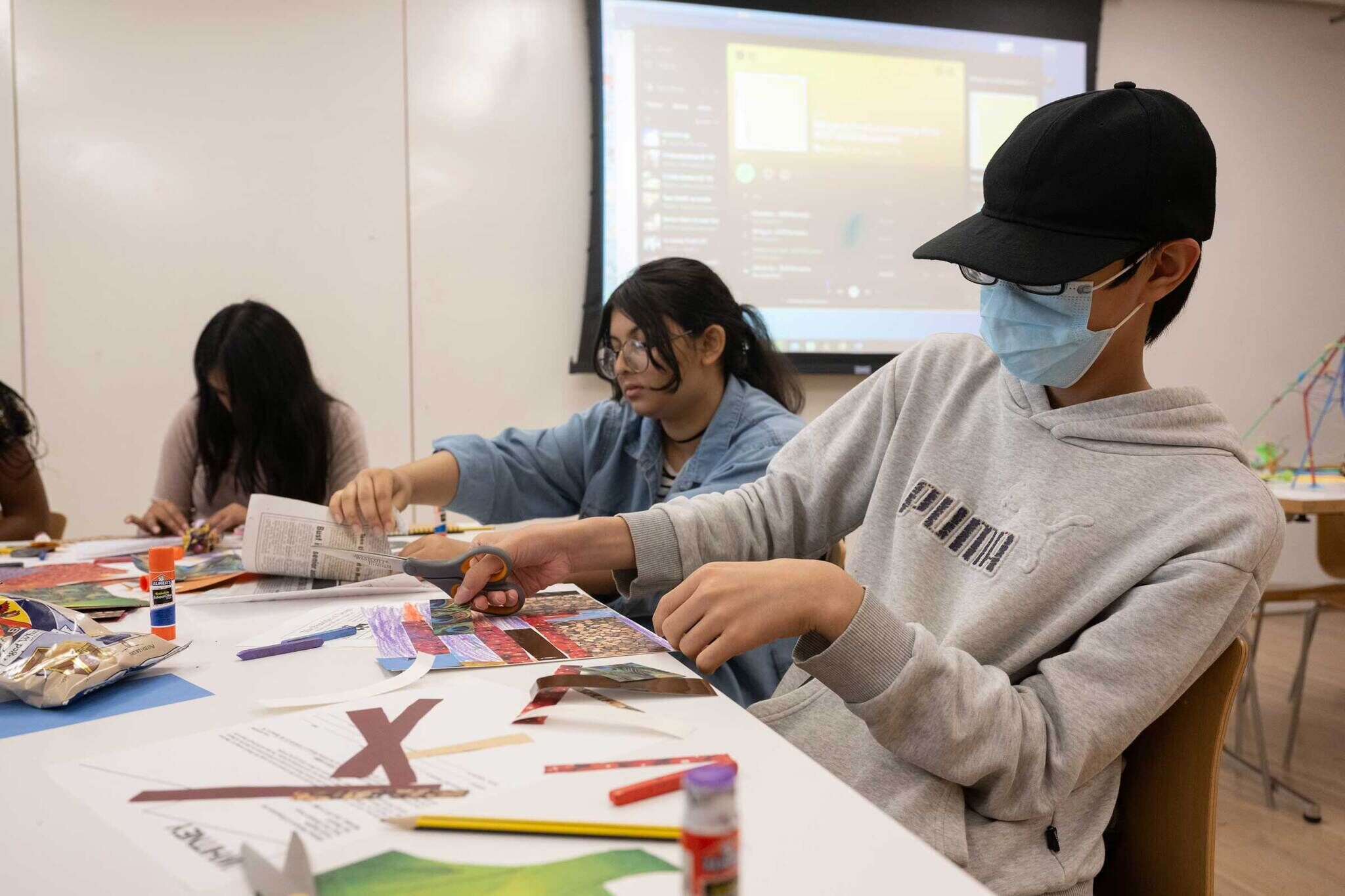 Three teens sit at a white table creating collage artwork.