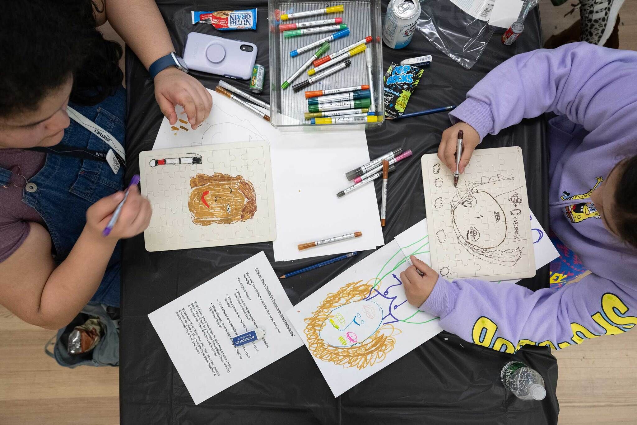 Birds-eye view of two teens sitting across from each other as they color with markers.