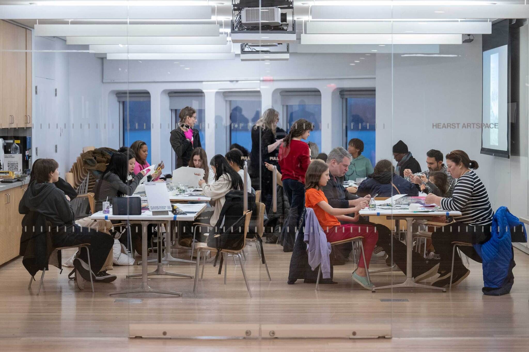 Group sits in a classroom, creating collage artwork. The photo shows a full landscape view of the teens working.