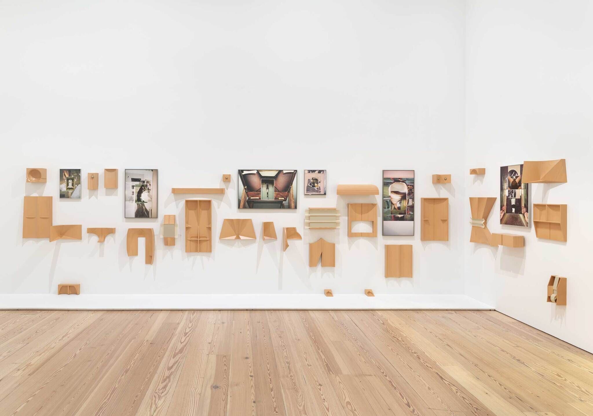 Modern art installation with photos and abstract wooden shapes on a white gallery wall.