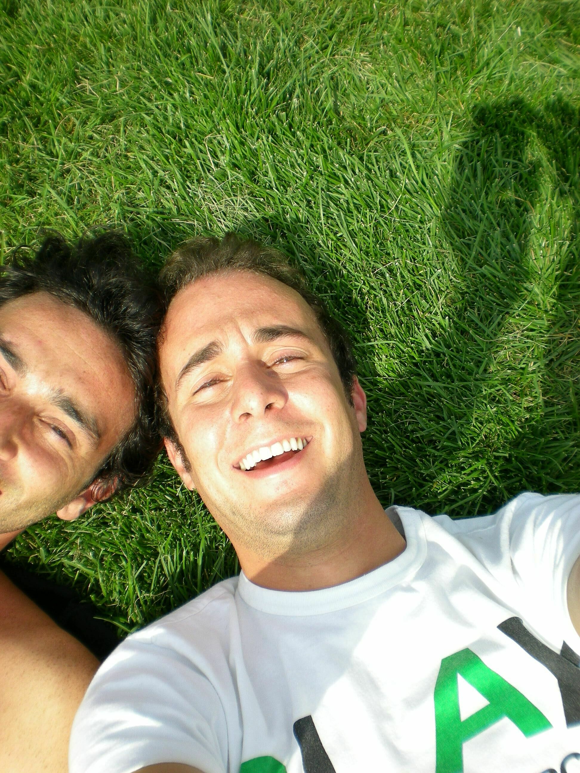 Photograph of a man and a friend taking a selfie in the grass.