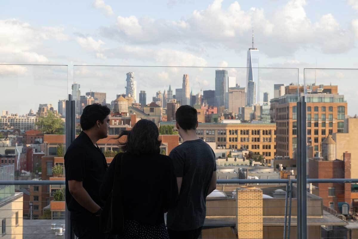 Three people looking at city skyline from outdoor terrace.