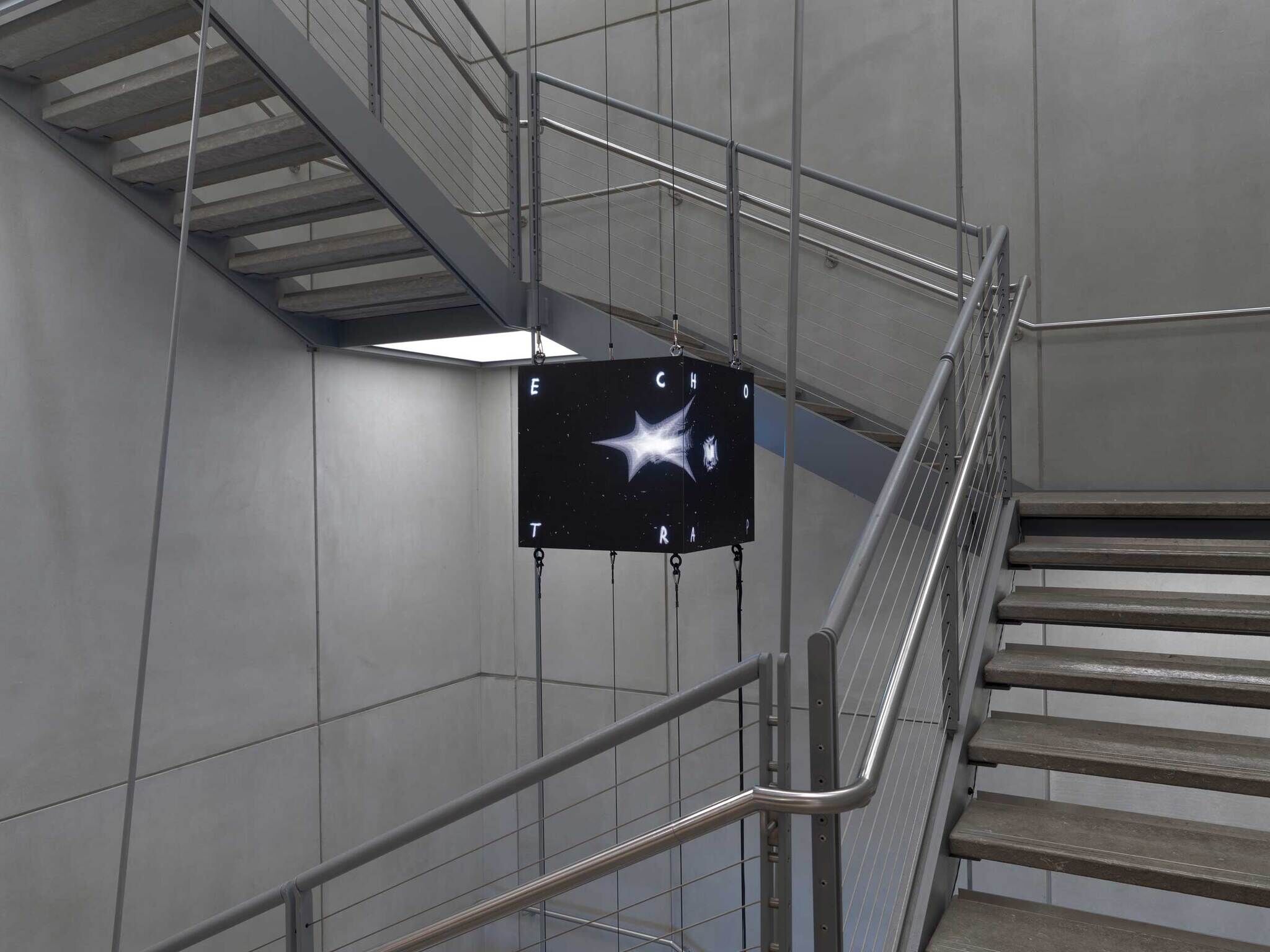 A digital display with a starry design hangs in a stairwell, showing the word "ECHO TRAP."