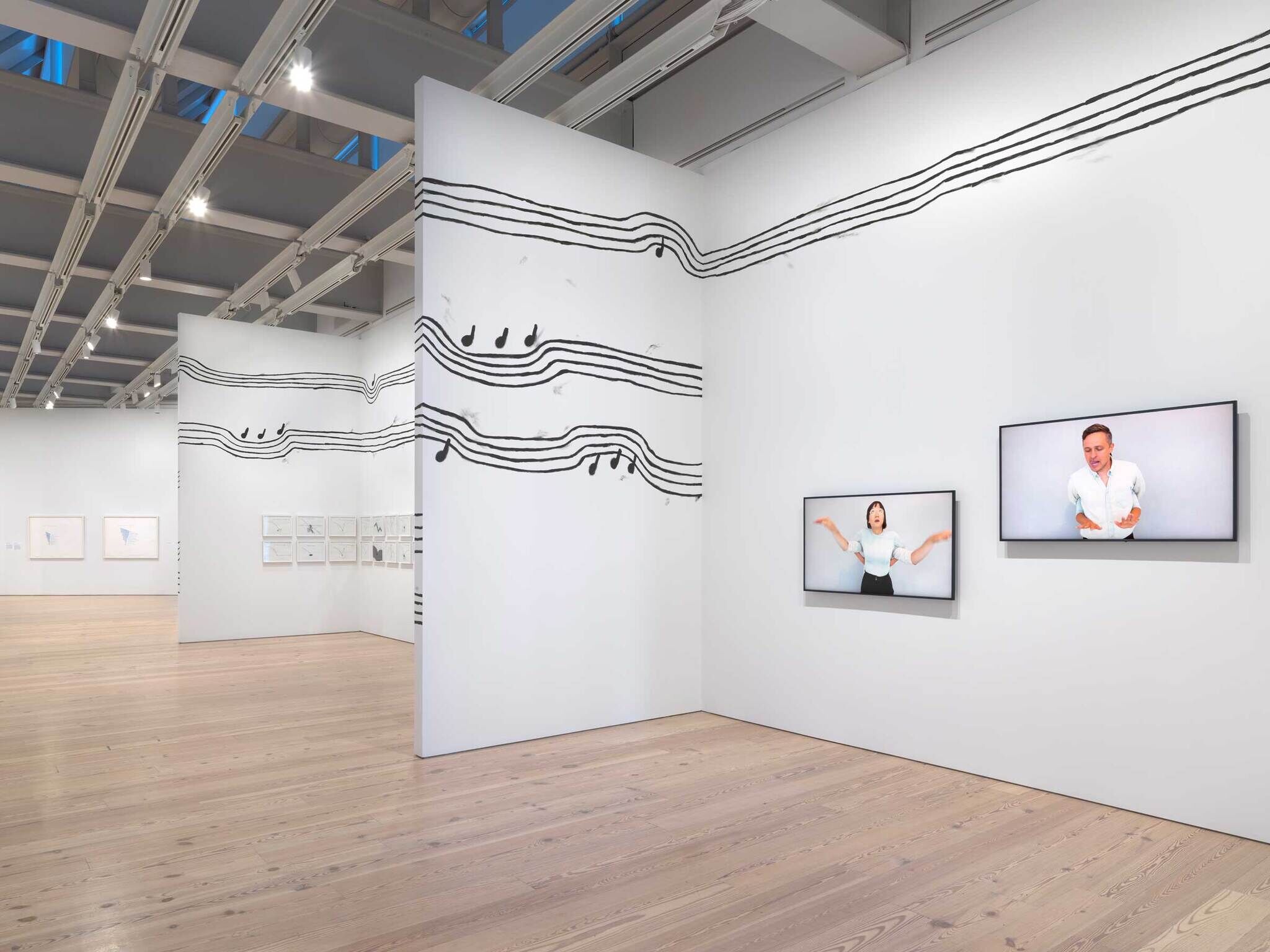 Art gallery with musical note wall design and two screens showing people gesturing expressively.