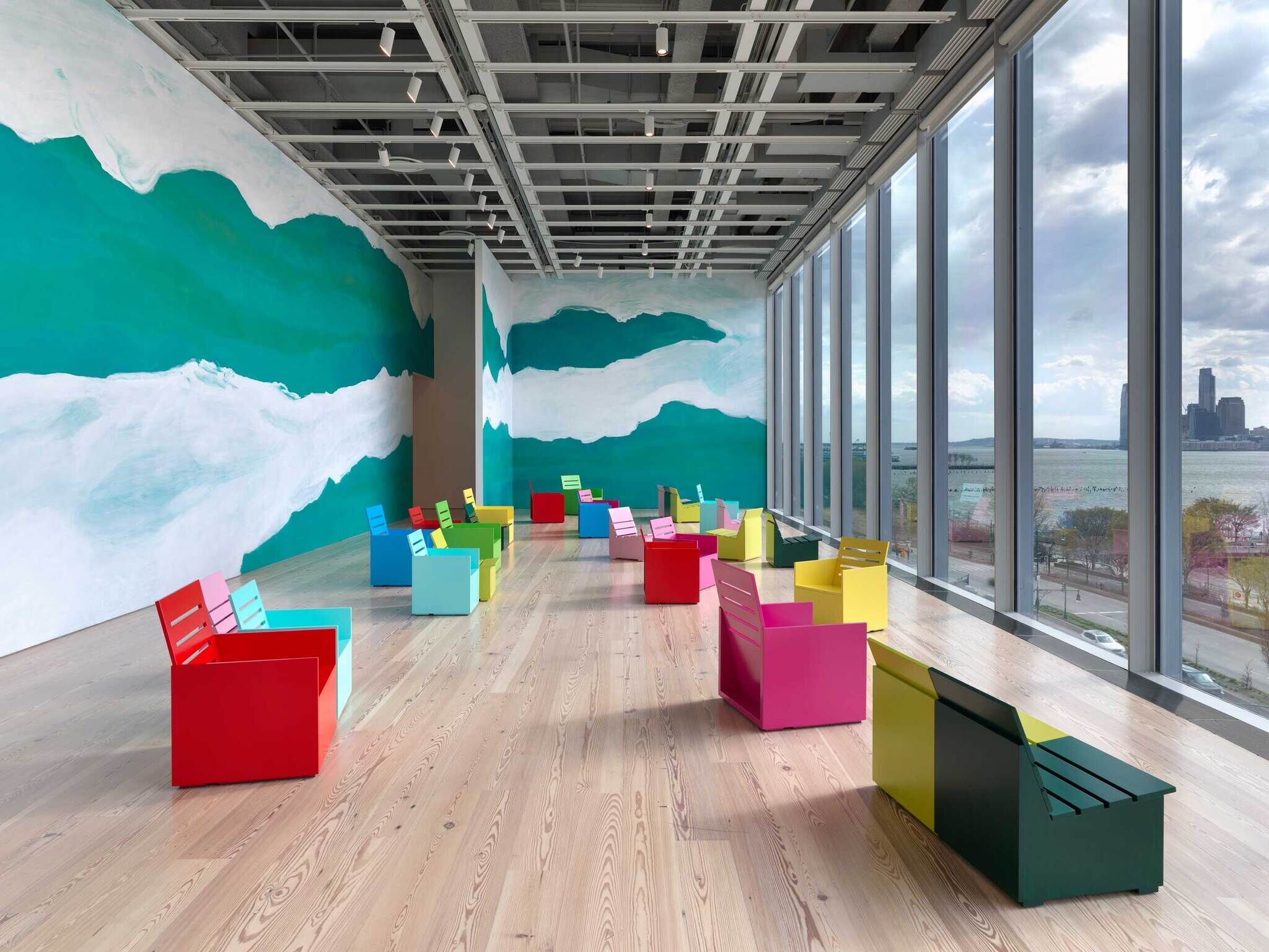 Brightly colored chairs are arranged in a spacious room with large windows and a green and white painted wall.