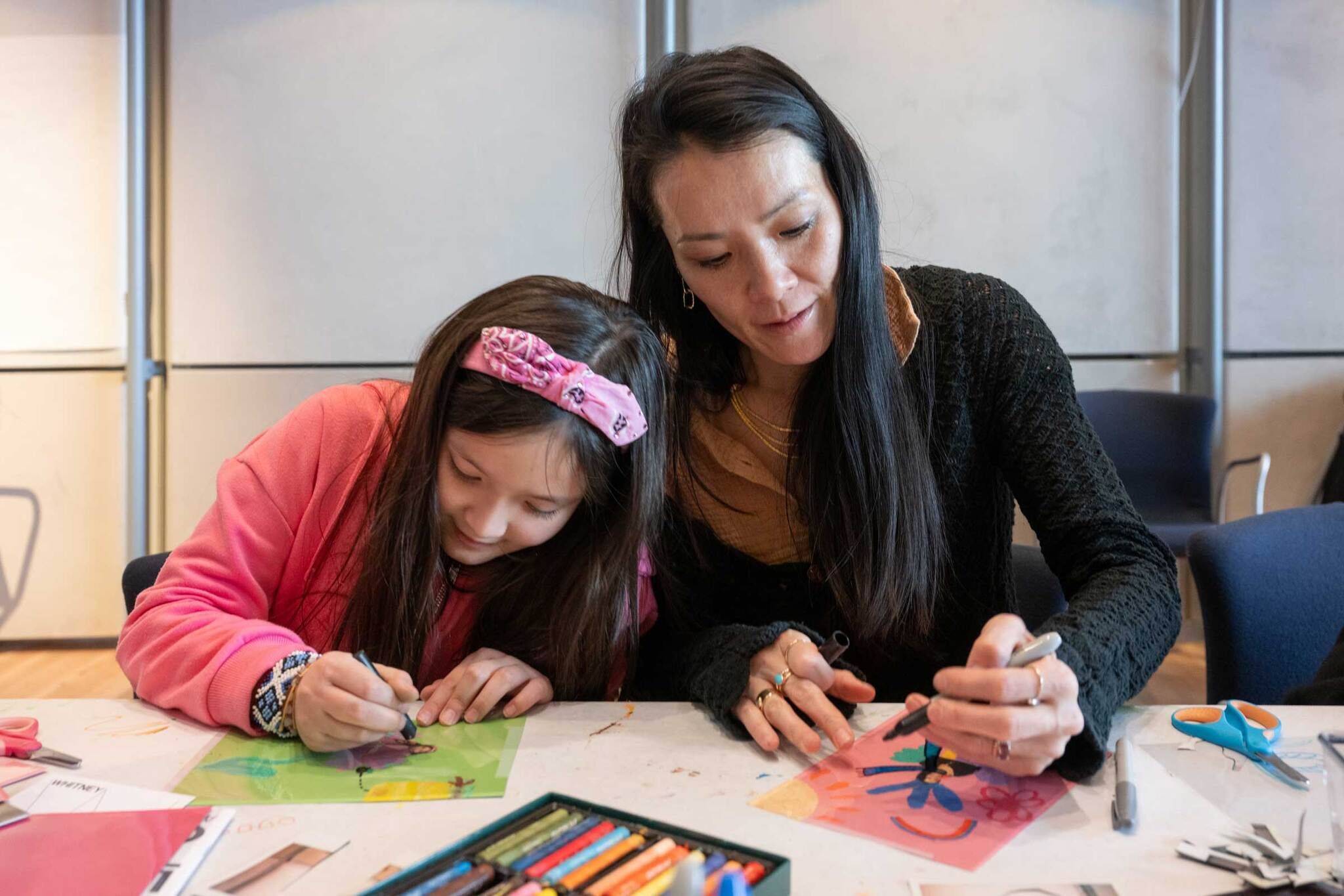 Two visitors, an adult and a child, create artwork together at a table during Second Sunday at the Whitney.
