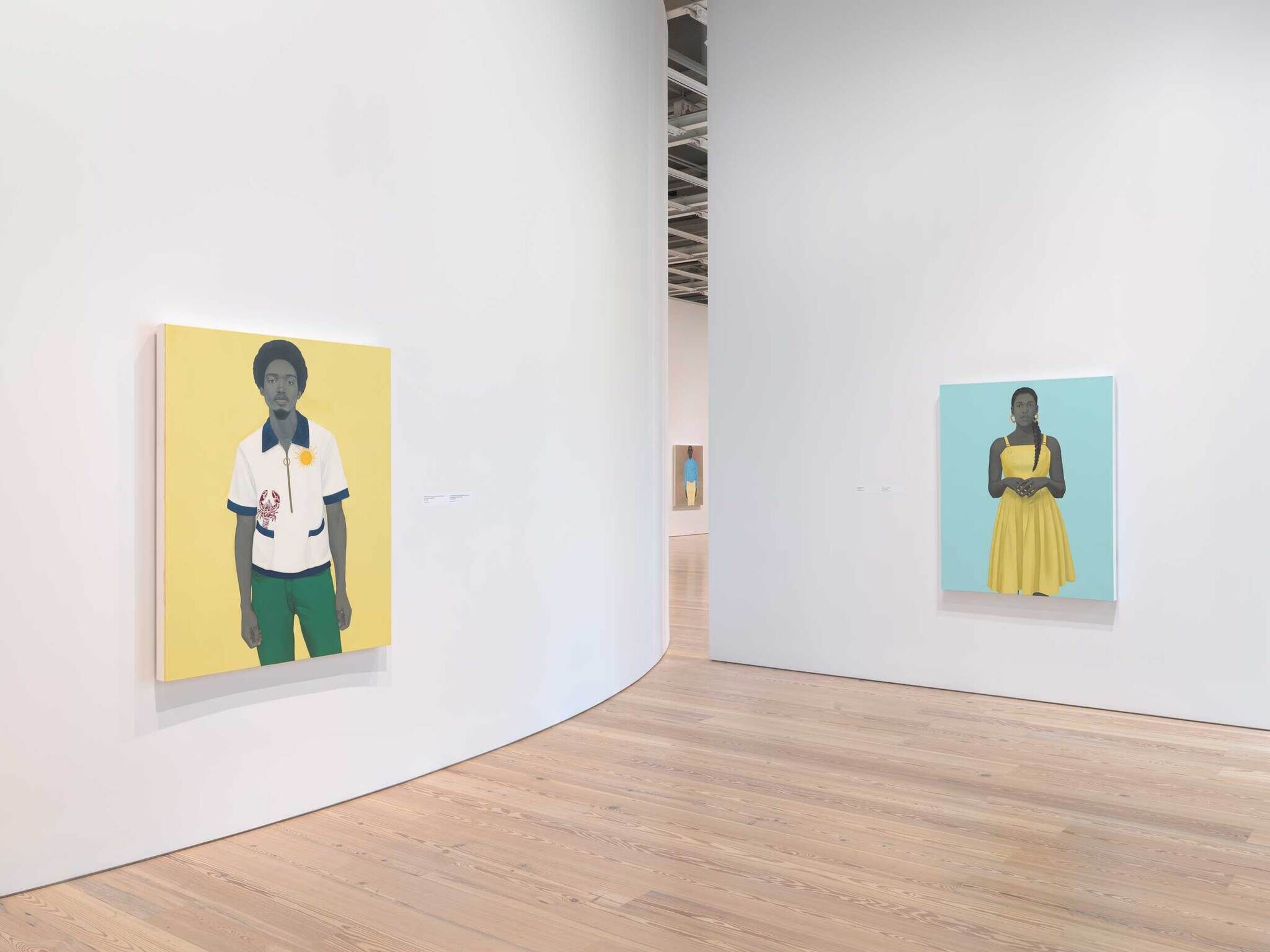Two colorful portraits of Black individuals hang on white walls in a modern art gallery with wooden floors.