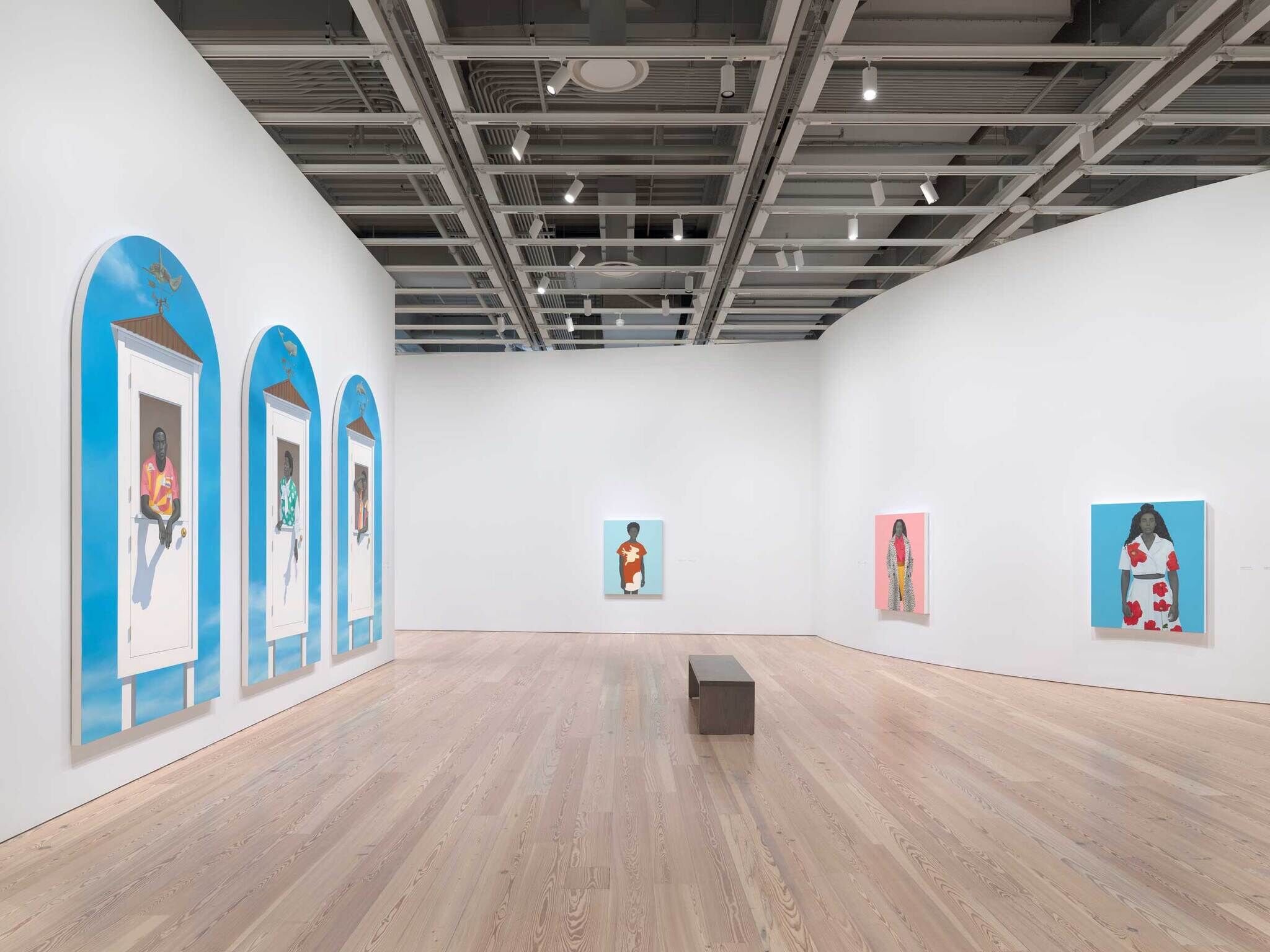 Art gallery with colorful portraits of people on white walls and a wooden bench in the center.