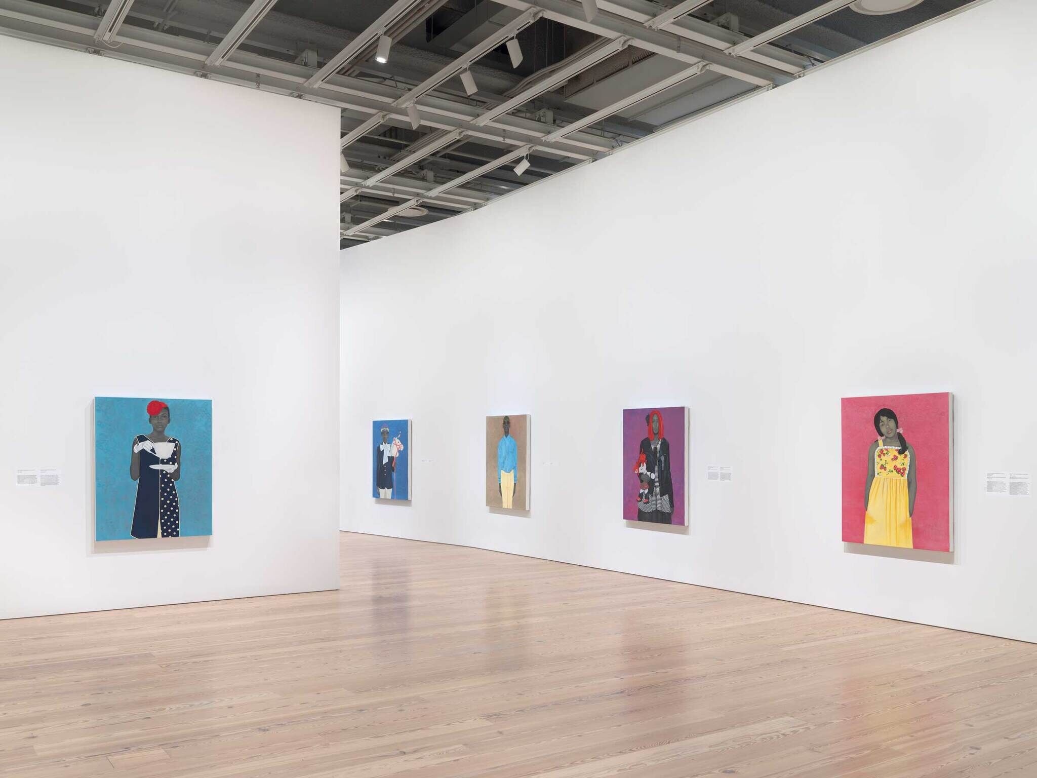 Art gallery with several colorful portraits of people hanging on white walls, each painting spaced evenly apart.