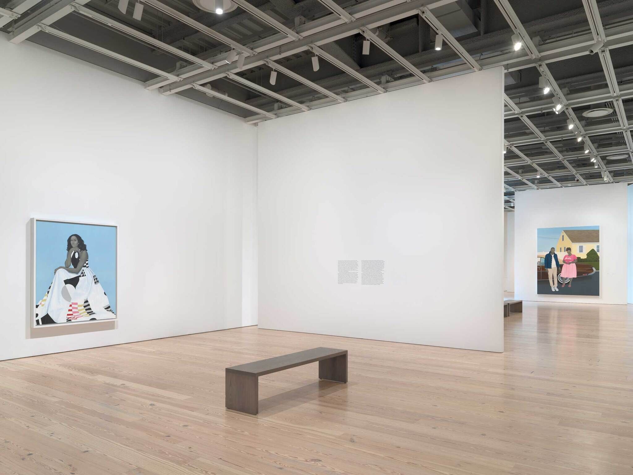 Art gallery with two large paintings on white walls and a simple wooden bench in the center.