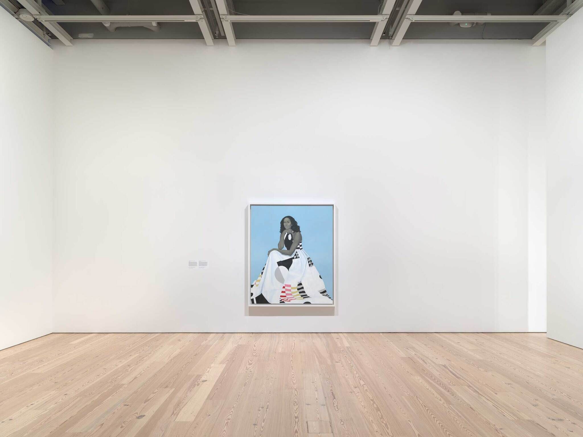 A framed painting of a seated woman hangs on a white wall in a spacious, empty art gallery.