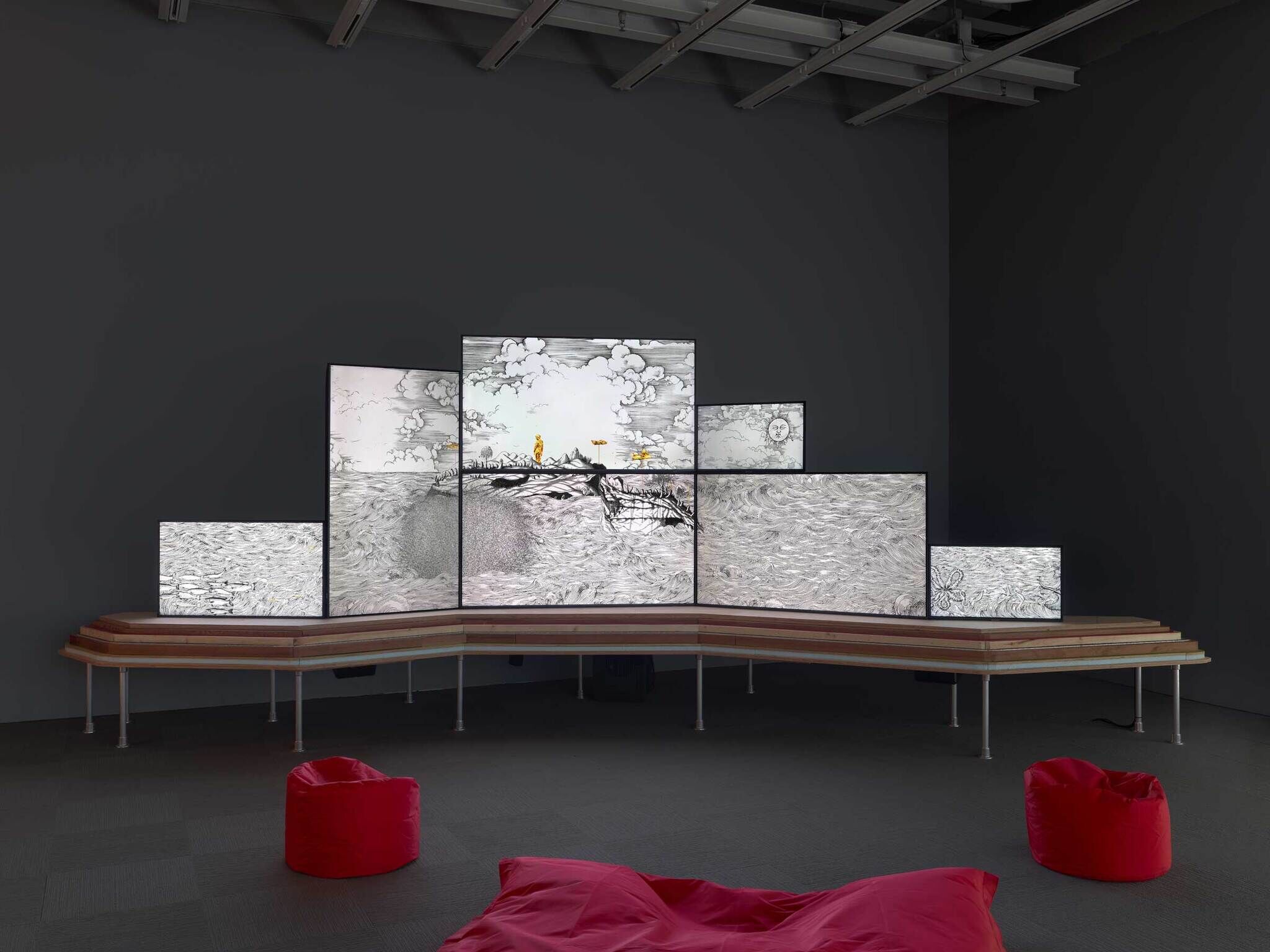 Several large screens display black and white animated drawings; red bean bag chairs are placed in front.