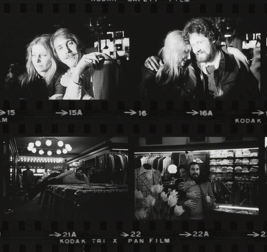 Two men and two women pose closely together in a clothing store, surrounded by racks of suits and shirts.