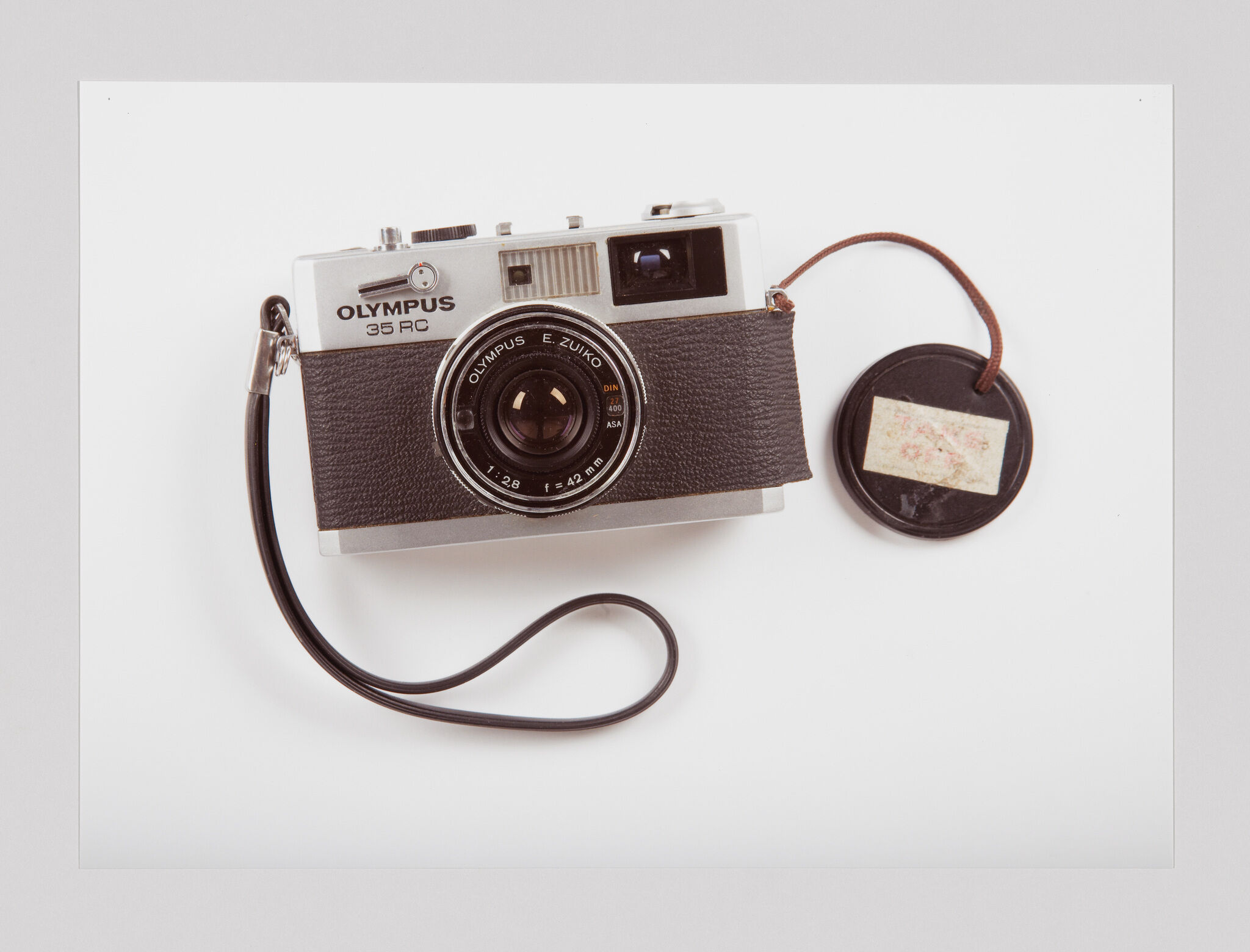 A vintage Olympus 35 RC film camera with a wrist strap and a lens cap attached by a string.