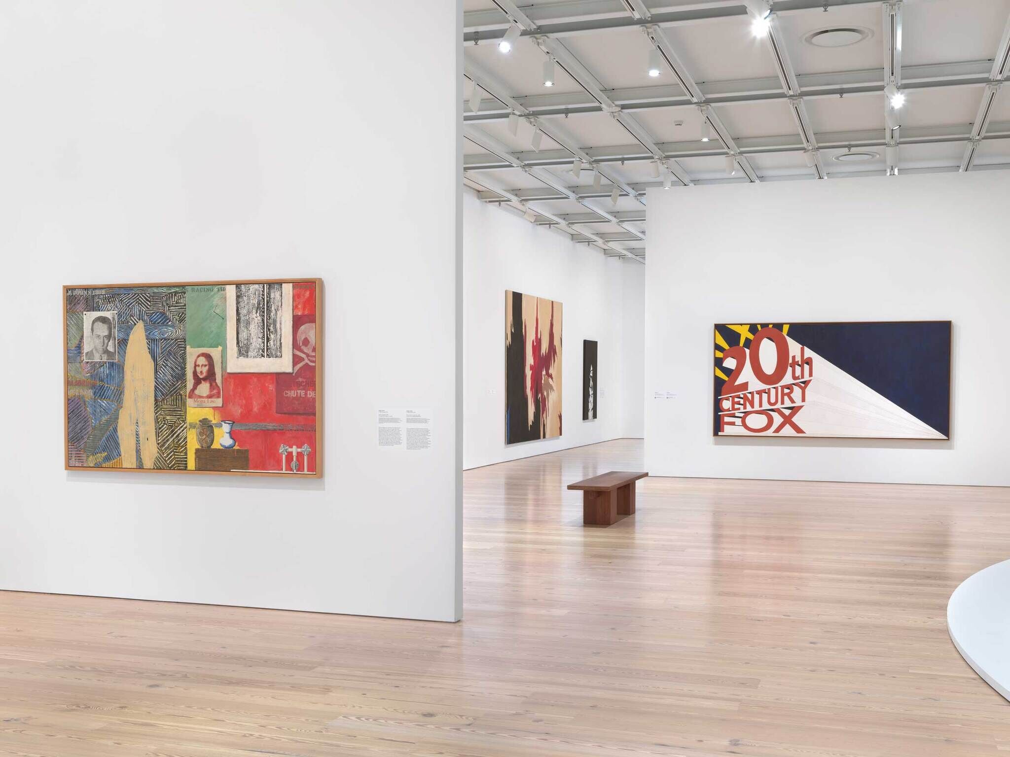 Art gallery with colorful modern paintings on white walls, including one with the text “20th Century Fox.”