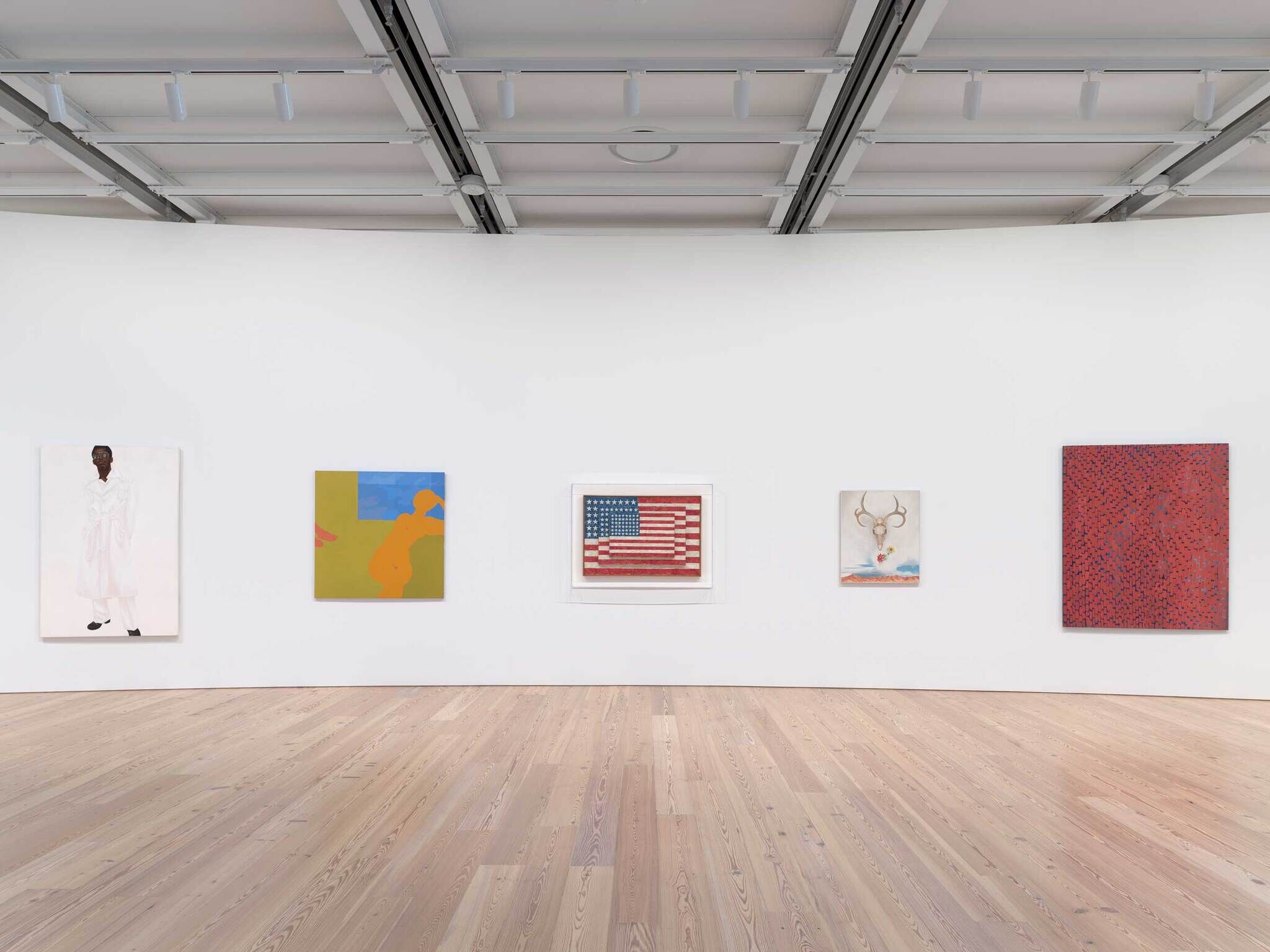 Five colorful paintings hang on a white gallery wall, including an American flag and abstract shapes.