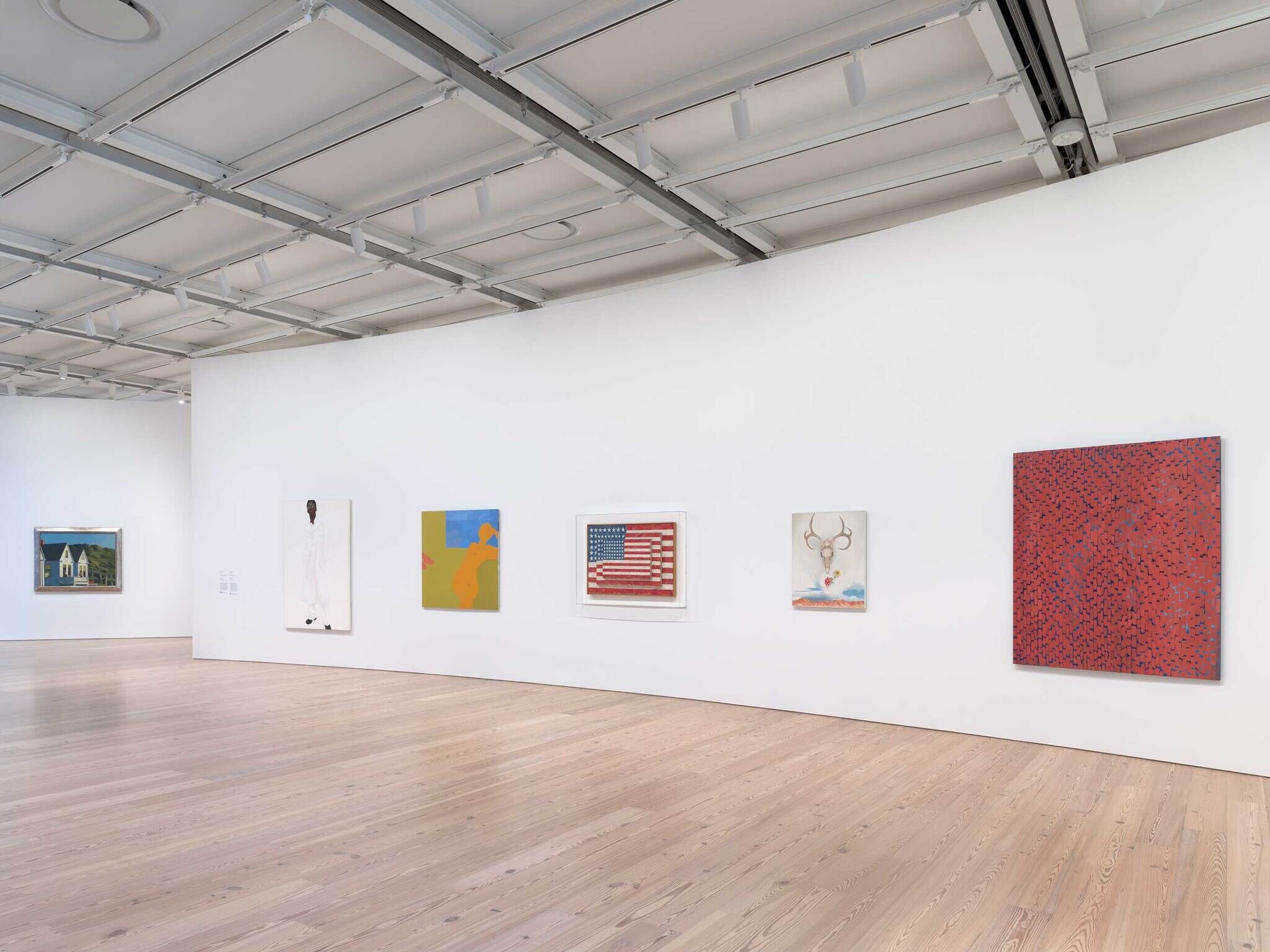 Six colorful paintings hang on a curved white wall in a spacious, modern art gallery with wooden floors.