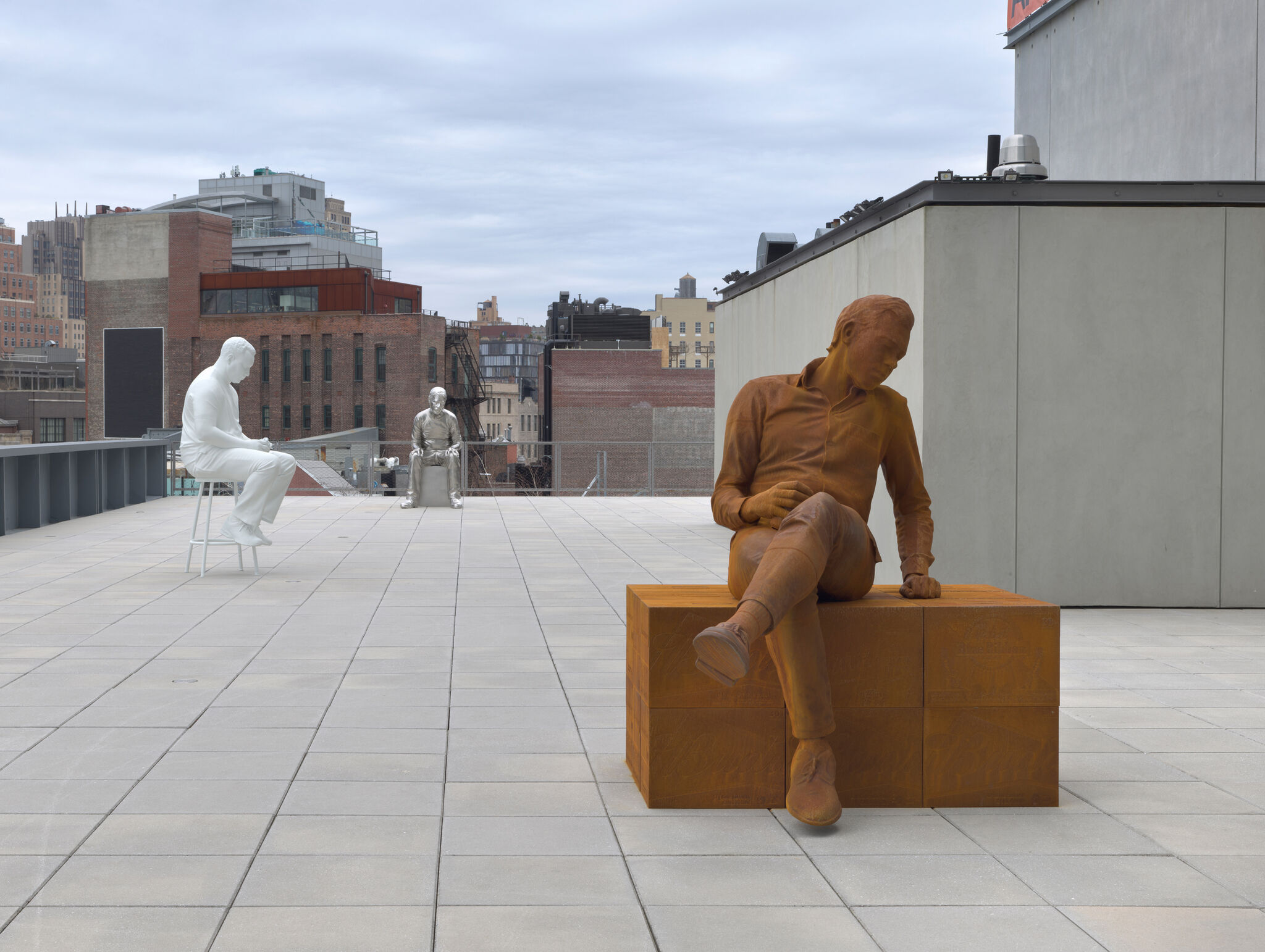 Three monochrome men sitting outside on a box or stool of the same color as them.