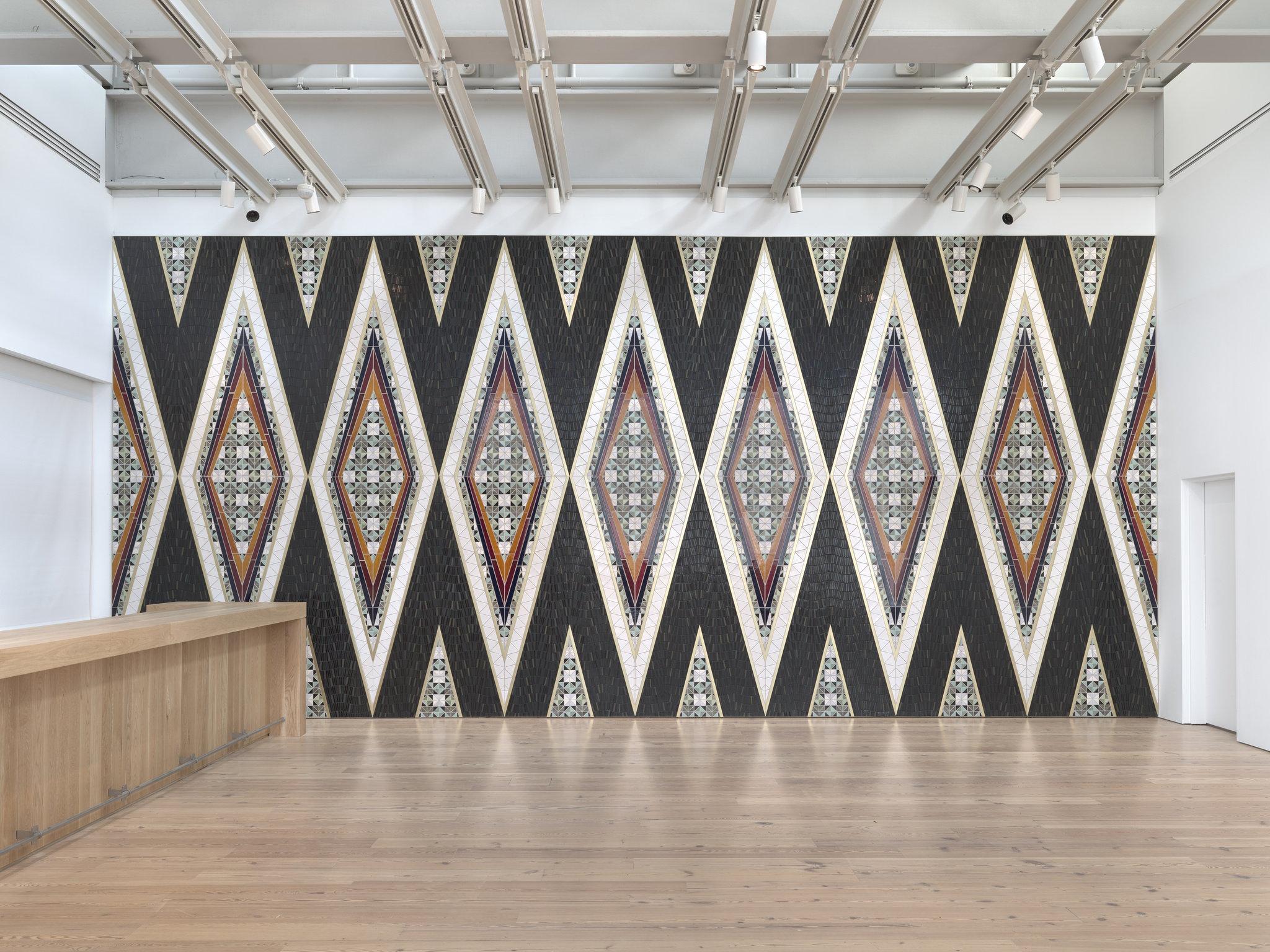 Large wall with repeating diamond-shaped patterns in black, white, and colorful mosaic designs, next to a wooden counter.