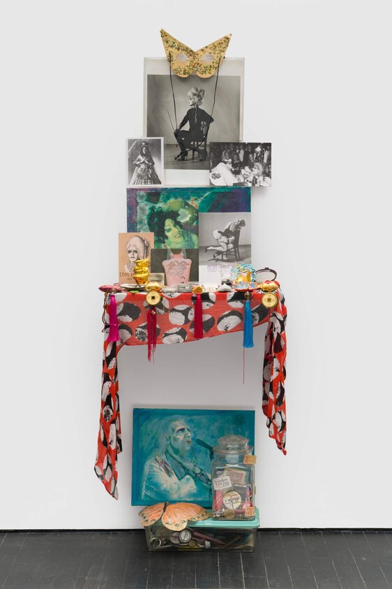 A colorful shrine with photos, a gold mask, small objects, and a painted portrait arranged on a shelf.